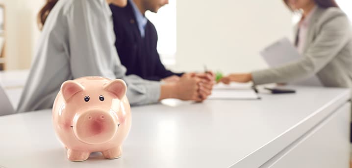 people sitting at a desk together to sign papers, with a piggy bank in the foreground