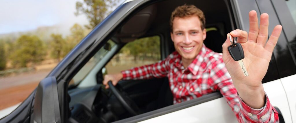 man smiling while holding the car key and sitting in new vehicle