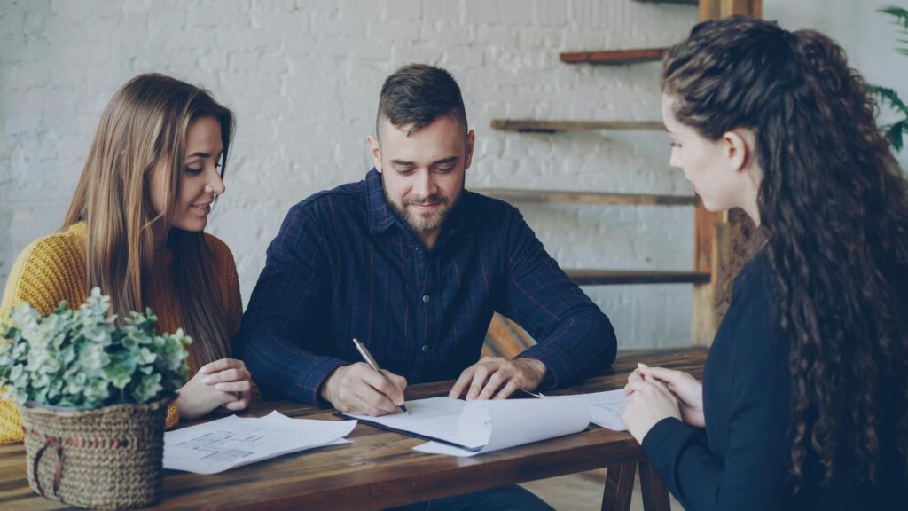 Young couple doing insurance paperwork with lady who is helping.