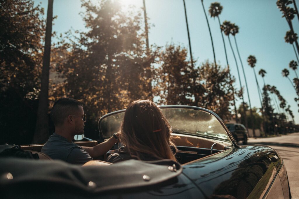 Couple driving in a car down a road with palm trees.