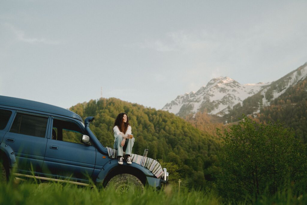 Women sitting on car hood with mountains in distance.