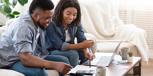 a couple smiling while using a calculator and laptop