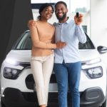 Couple standing together in front of a car smiling and holding the keys