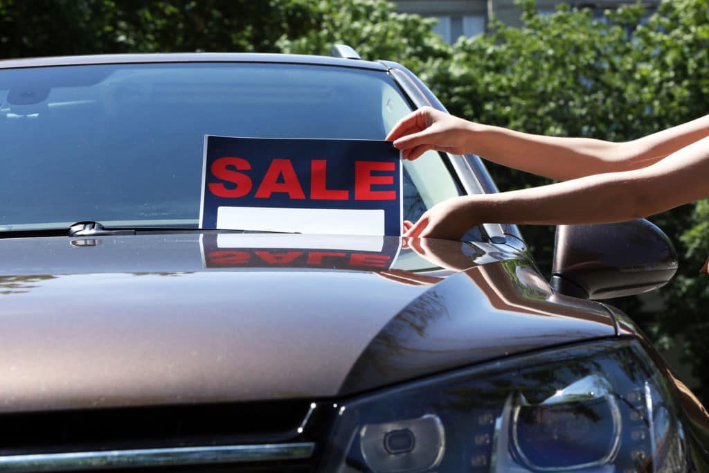 Photo of hands placing a for sale sign on the windshield of a car that is parked