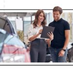 Two individuals standing next to a car, reviewing documents