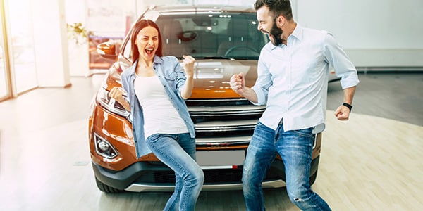 happy young couple standing in front of a new car