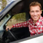 man smiling while holding the car key and sitting in new vehicle