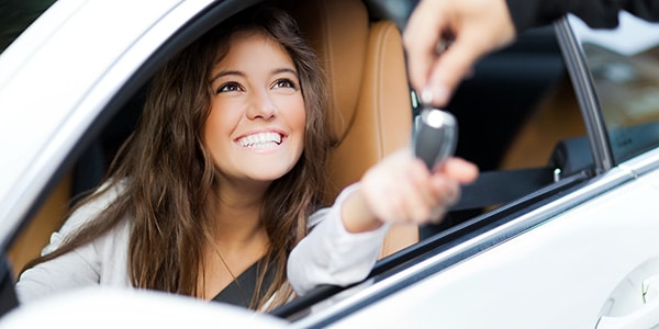 woman sitting in the drivers seat of a car smiling while being given keys to her new car