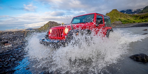 Red jeep wrangler splashing through water