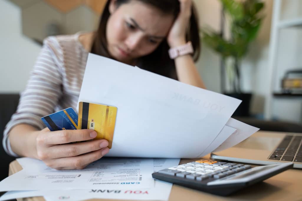 Woman looking frustrated and looking at bills while sitting at a table with her head in her hand