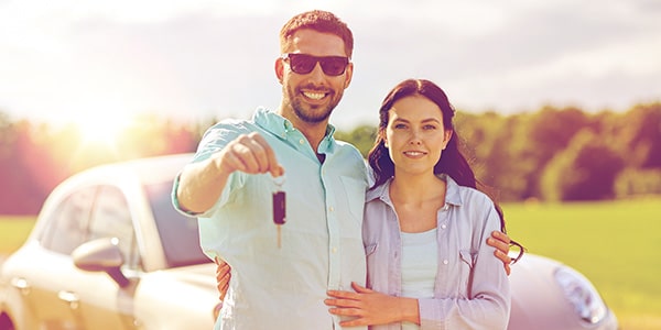 smiling couple standing in front of a new car holding the car keys