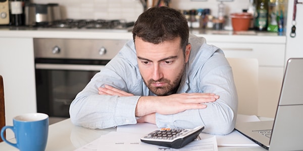 man looking upset while sitting at his desk near a computer and calculator