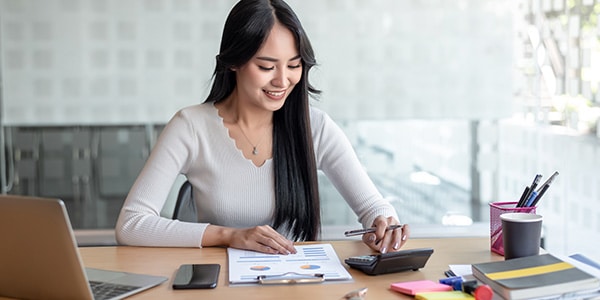 woman sitting at desk, using a calculator and smiling